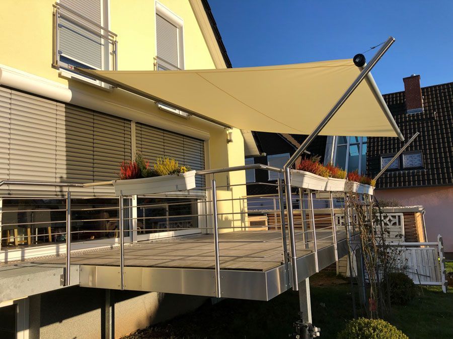 Ein Balkon mit einer weissen Markise darüber und einem gelben Haus im Hintergrund