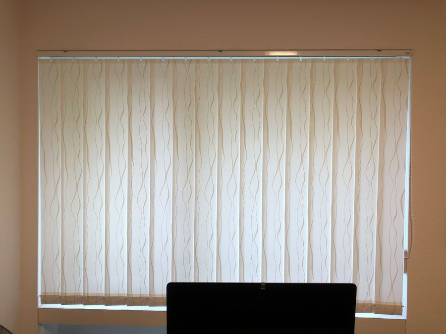 Ein Computer steht vor einem Fenster mit Vertikaljalousien.