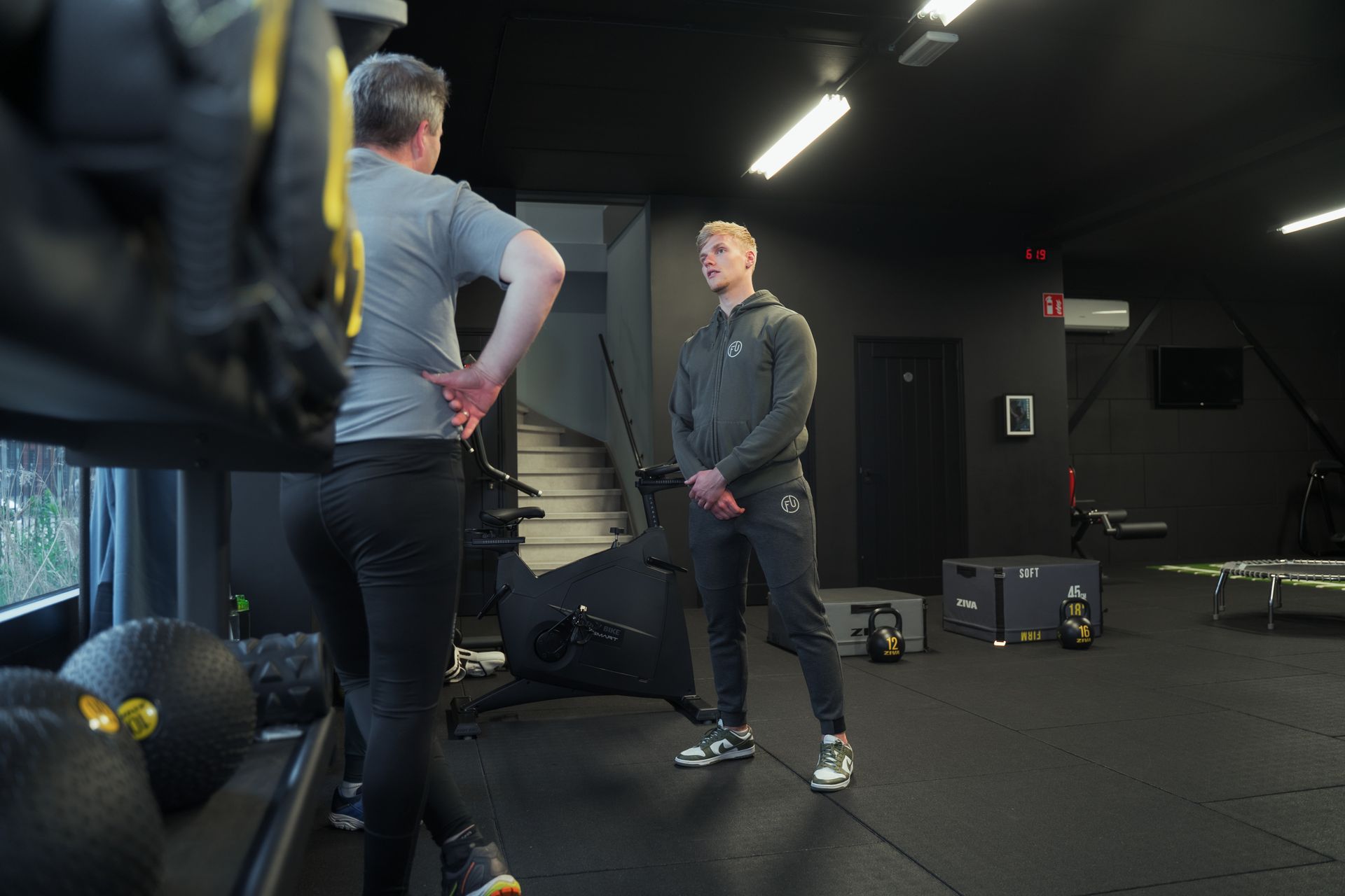 Twee mannen staan in een sportschool met elkaar te praten.