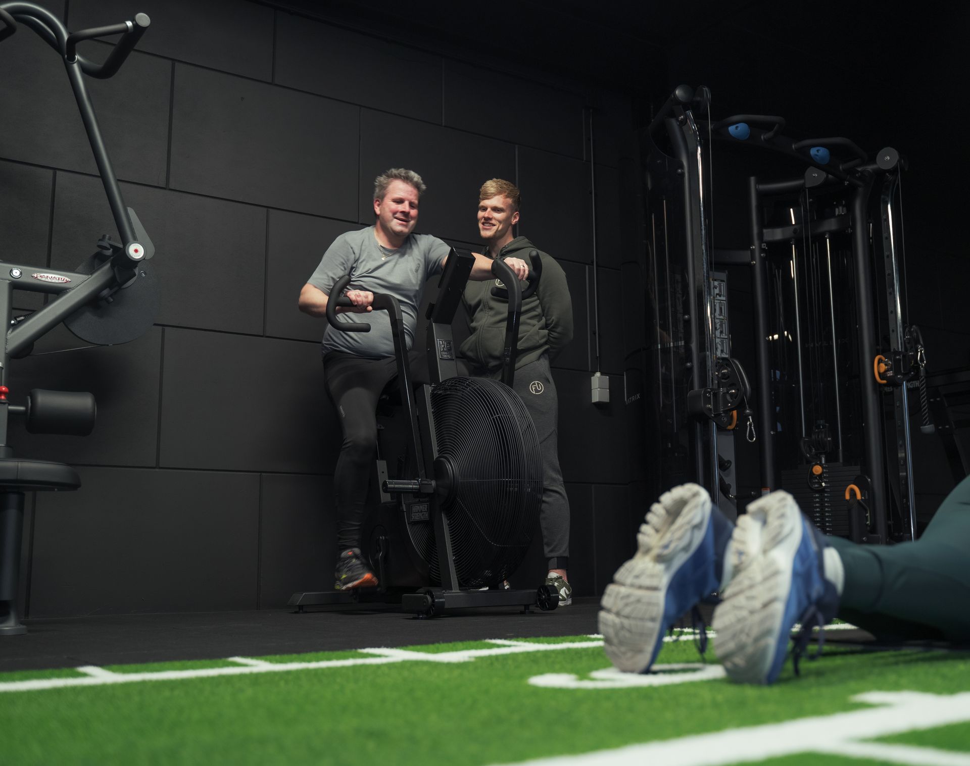 Een man zit op een cardio machine terwijl de personal trainer toekijkt.