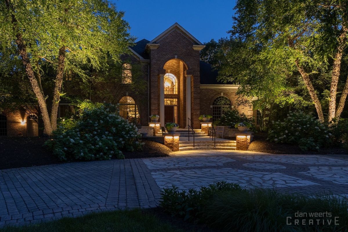 A large brick house is lit up at night with trees in front of it.
