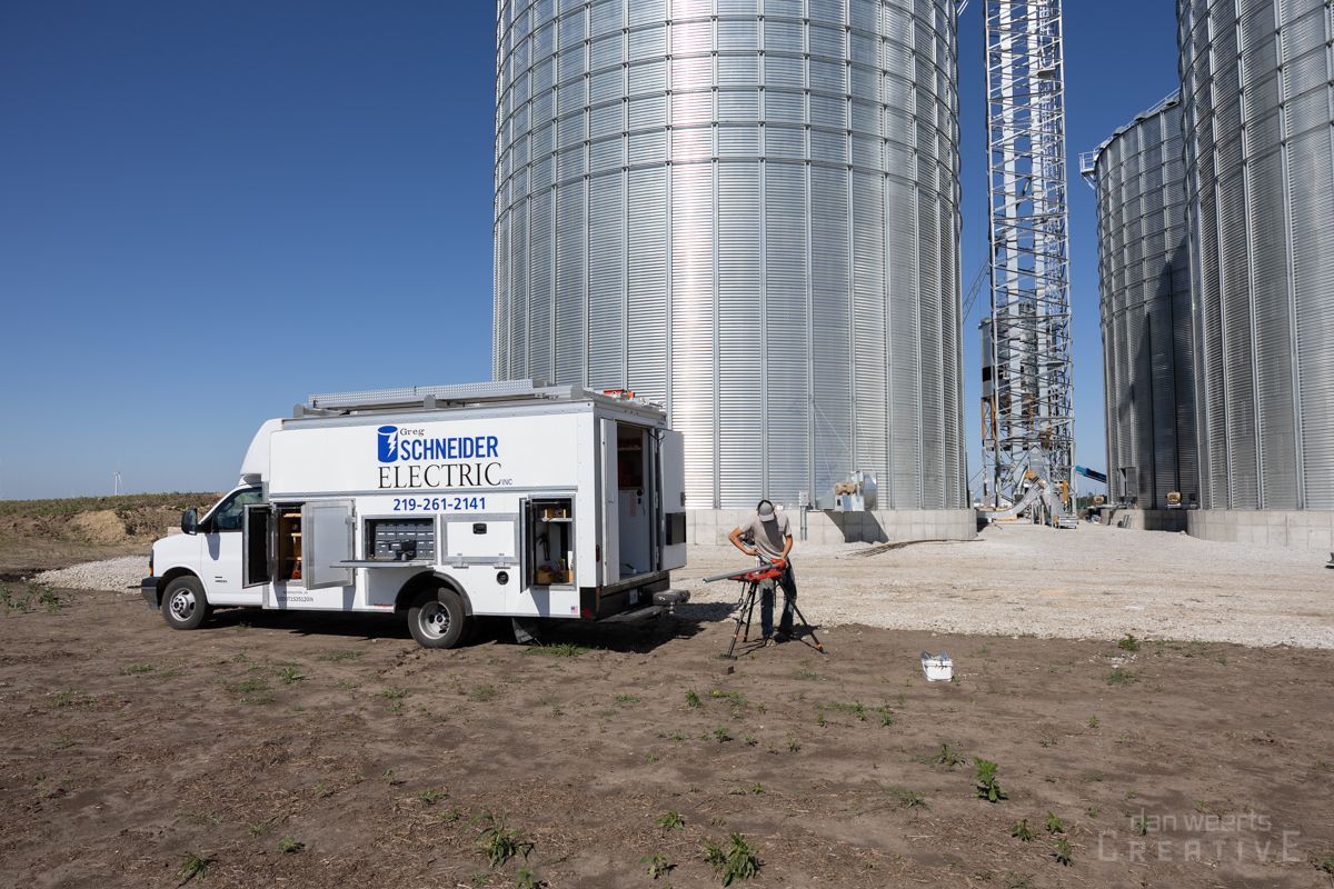 A white van is parked in front of a row of silos.