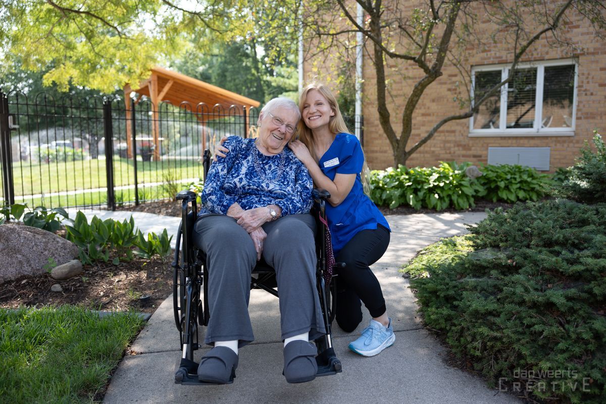 A woman is standing next to an elderly woman in a wheelchair.