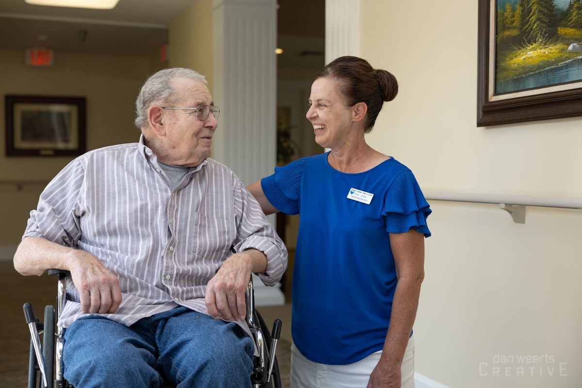 A woman is standing next to an elderly man in a wheelchair.