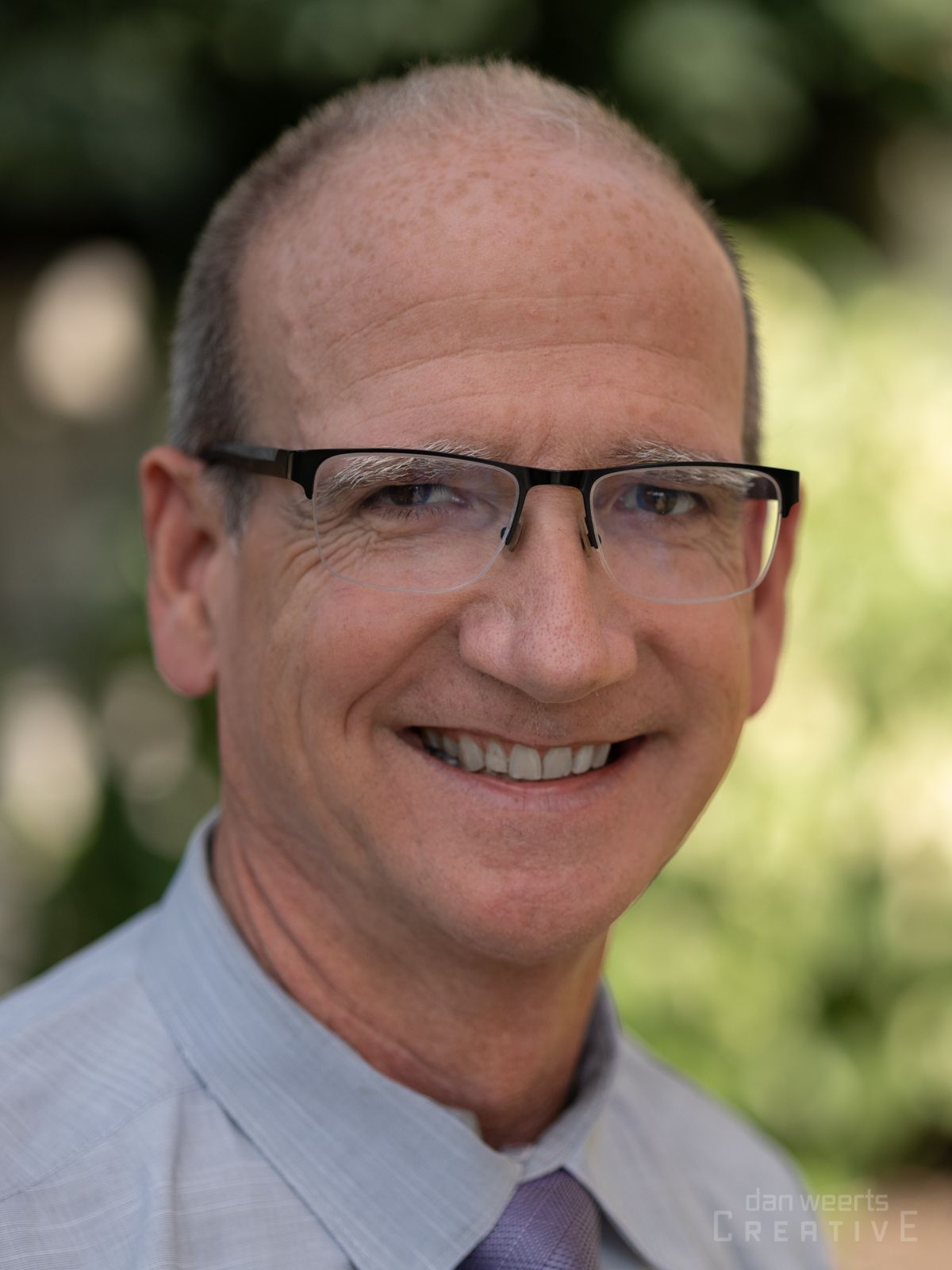 A man wearing glasses and a tie is smiling for the camera.
