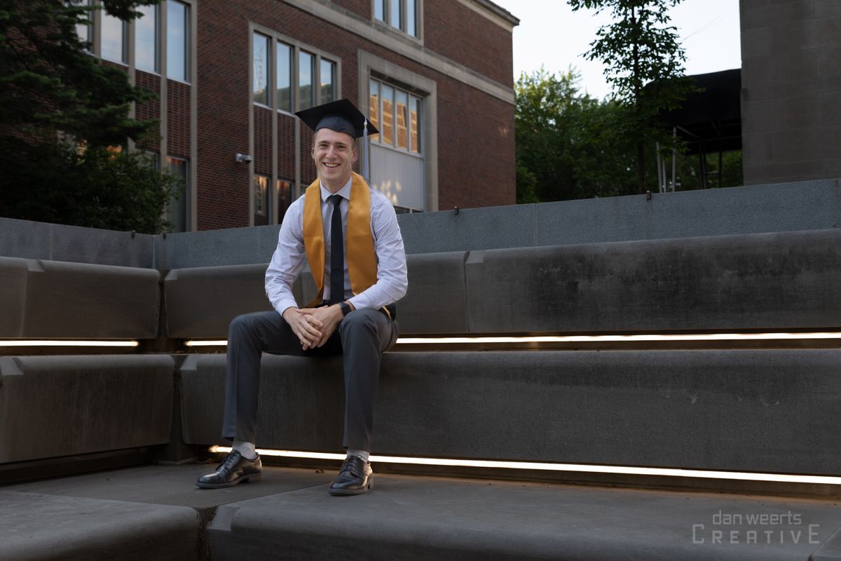 A man in a graduation cap and gown is sitting on steps