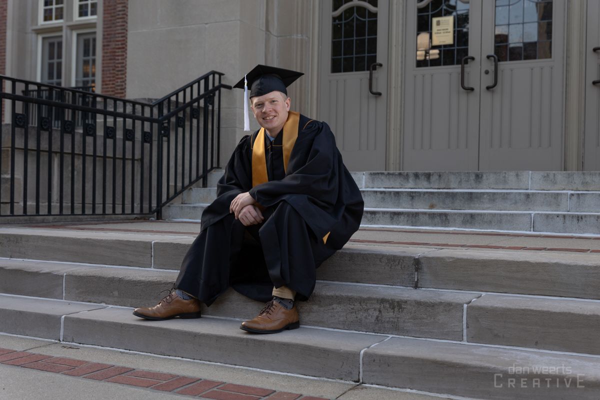 A man in a graduation cap and gown is sitting on the steps of a building.