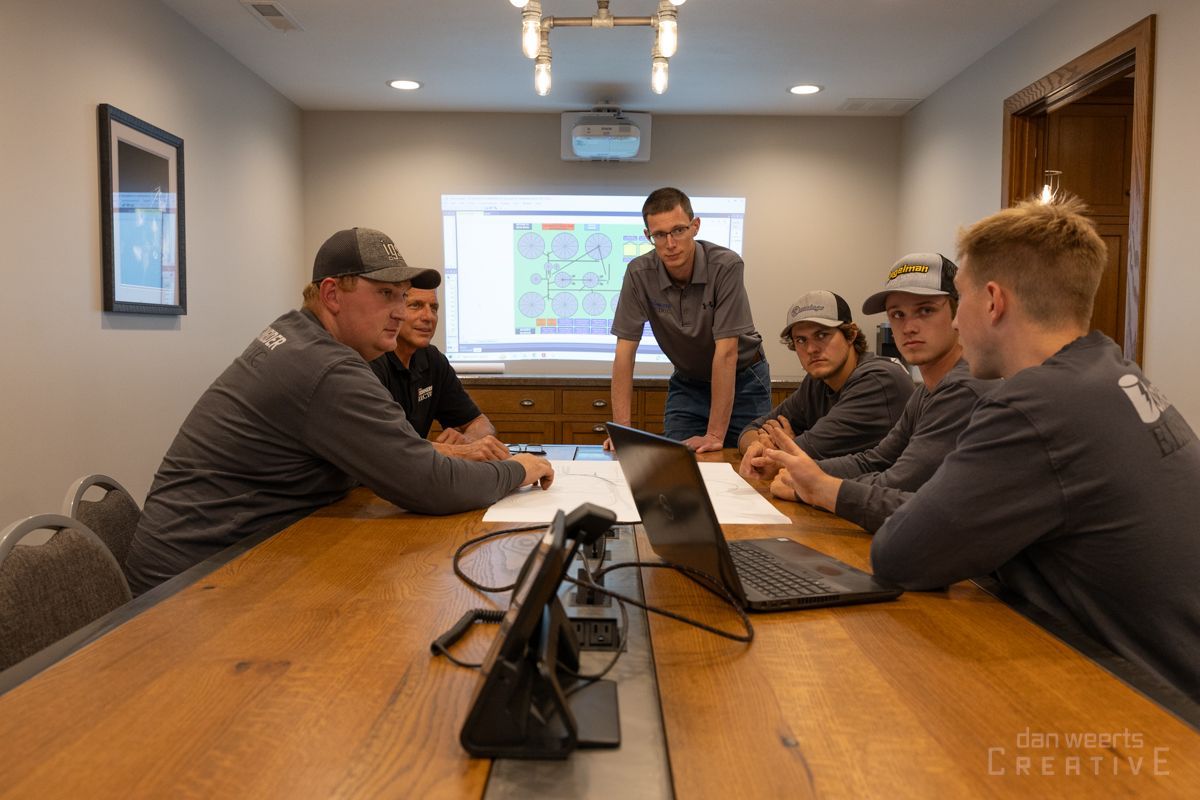A group of men are sitting around a table with laptops in a conference room.