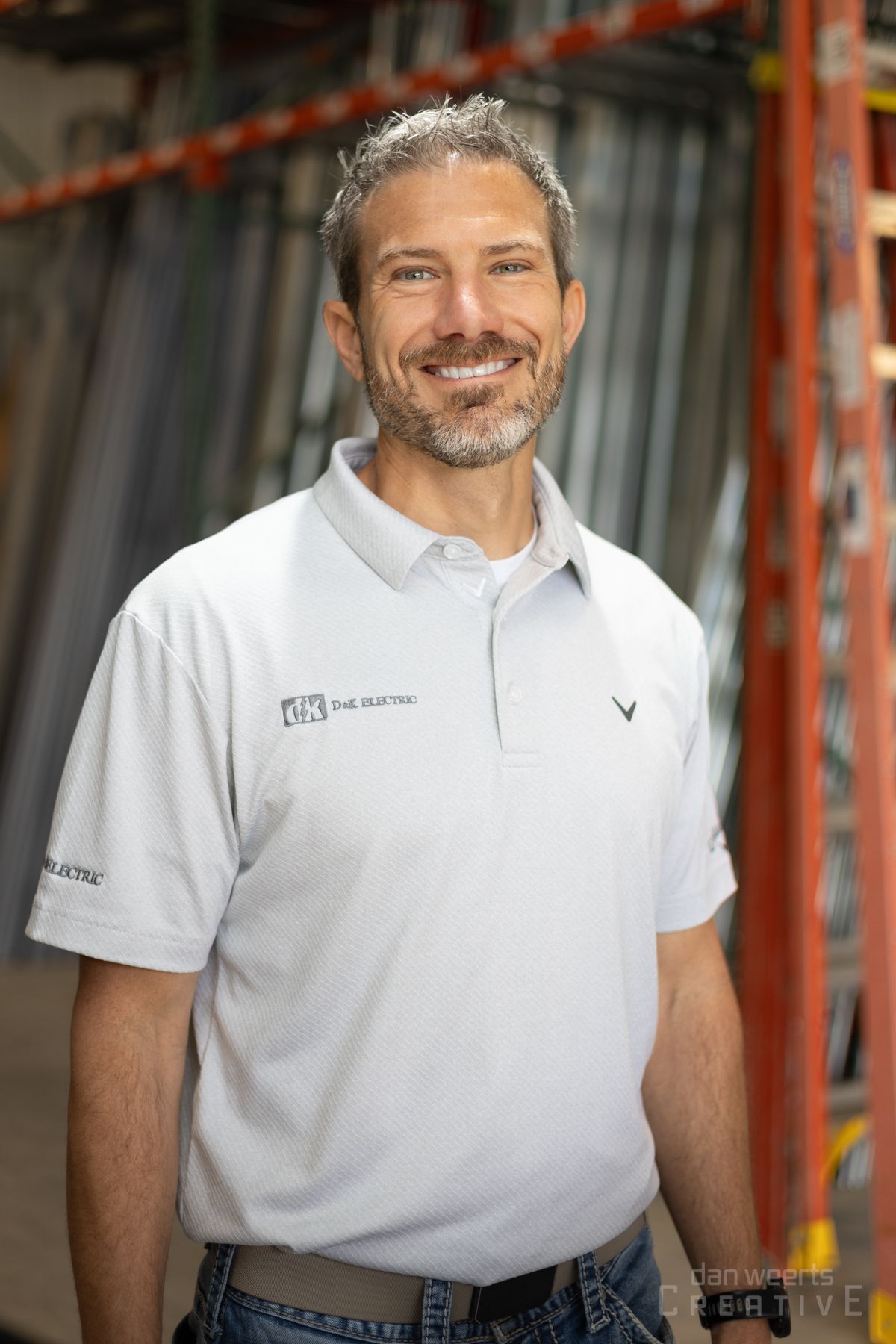 A man with a beard is wearing a white polo shirt and jeans.