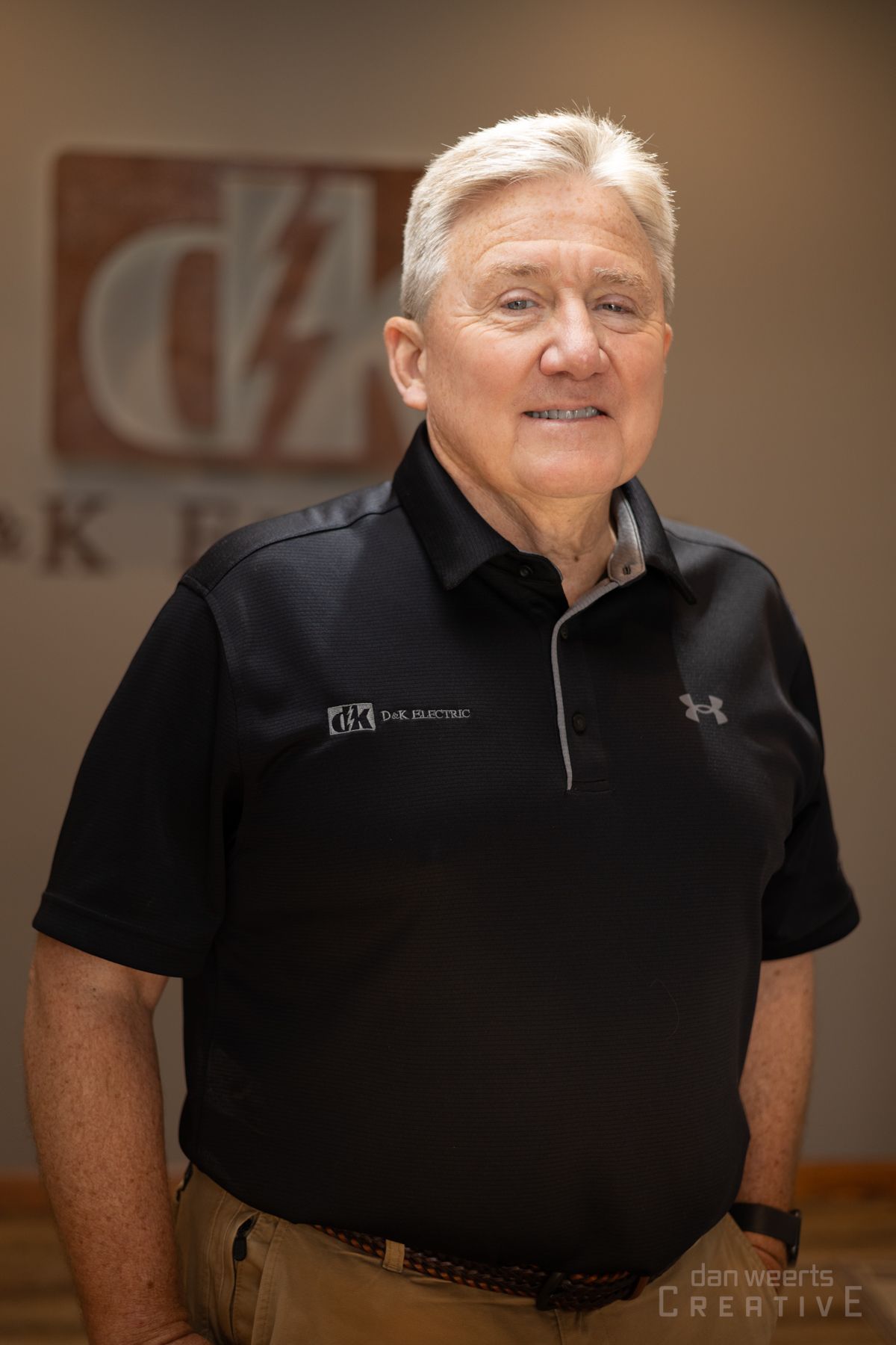 A man wearing a black shirt and khaki pants is standing in front of a sign.