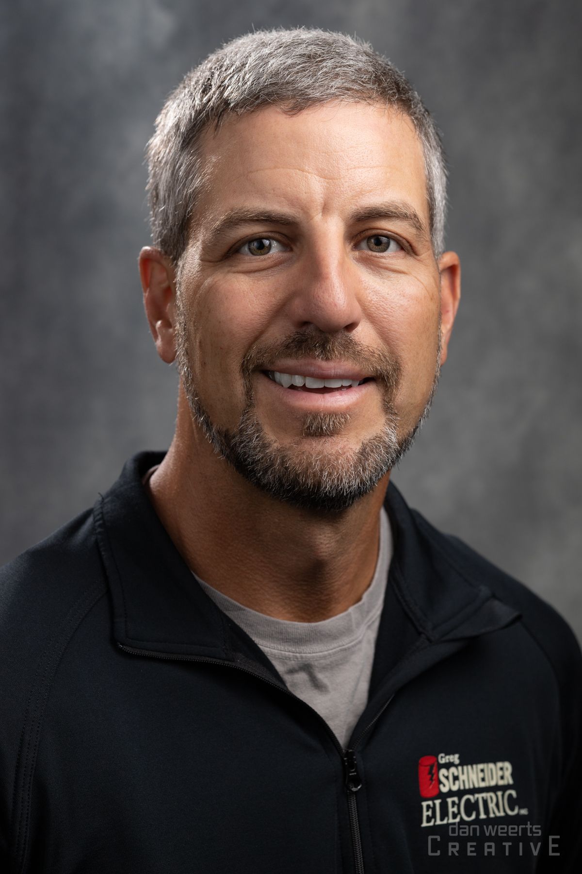 A man with a beard and a black jacket is smiling for the camera.