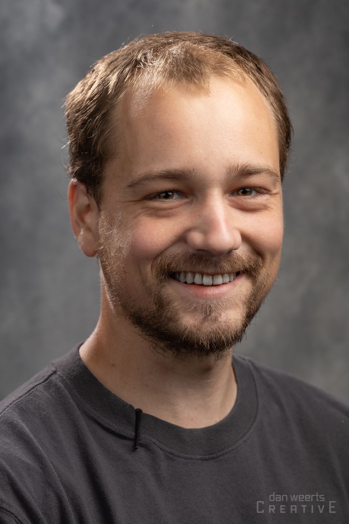 A man with a beard is smiling for the camera while wearing a black shirt.