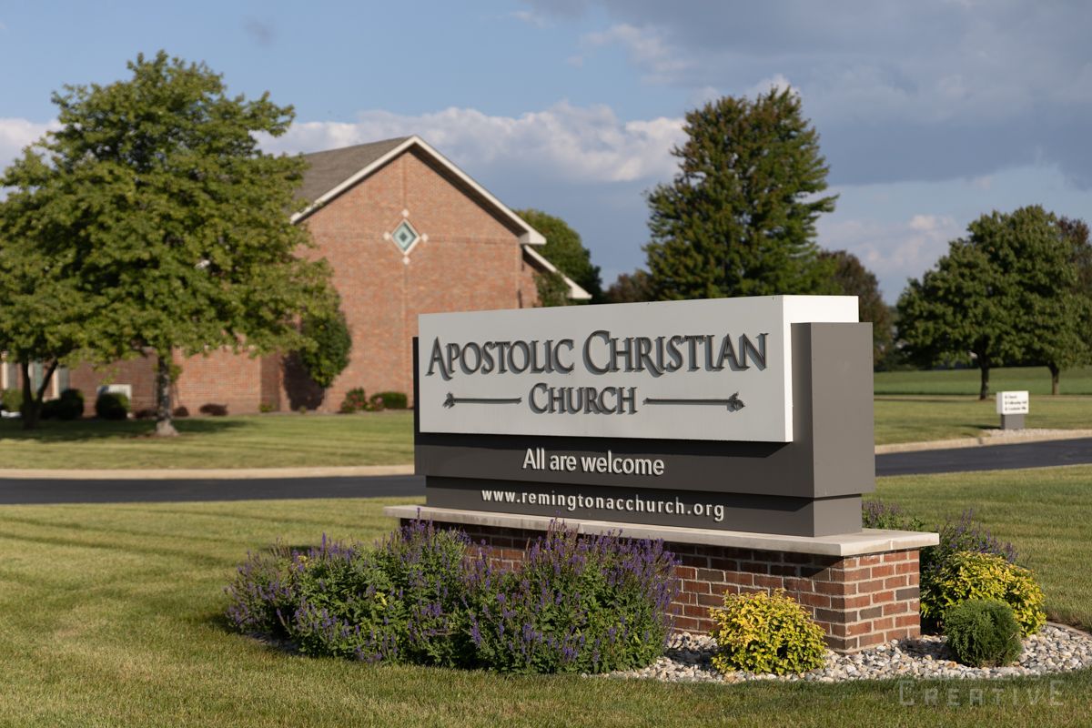 A sign for the apostolic christian church is in front of a brick building