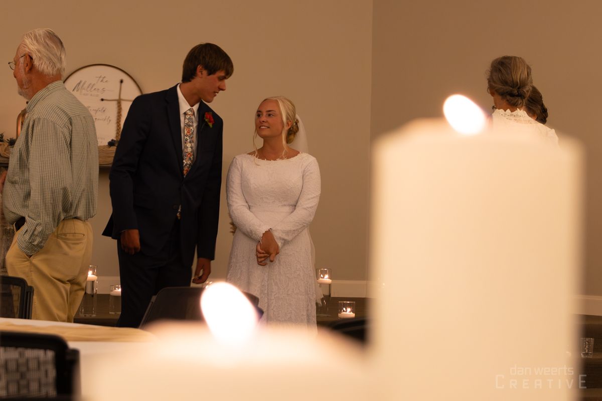 A bride and groom are standing next to each other in a church surrounded by candles.