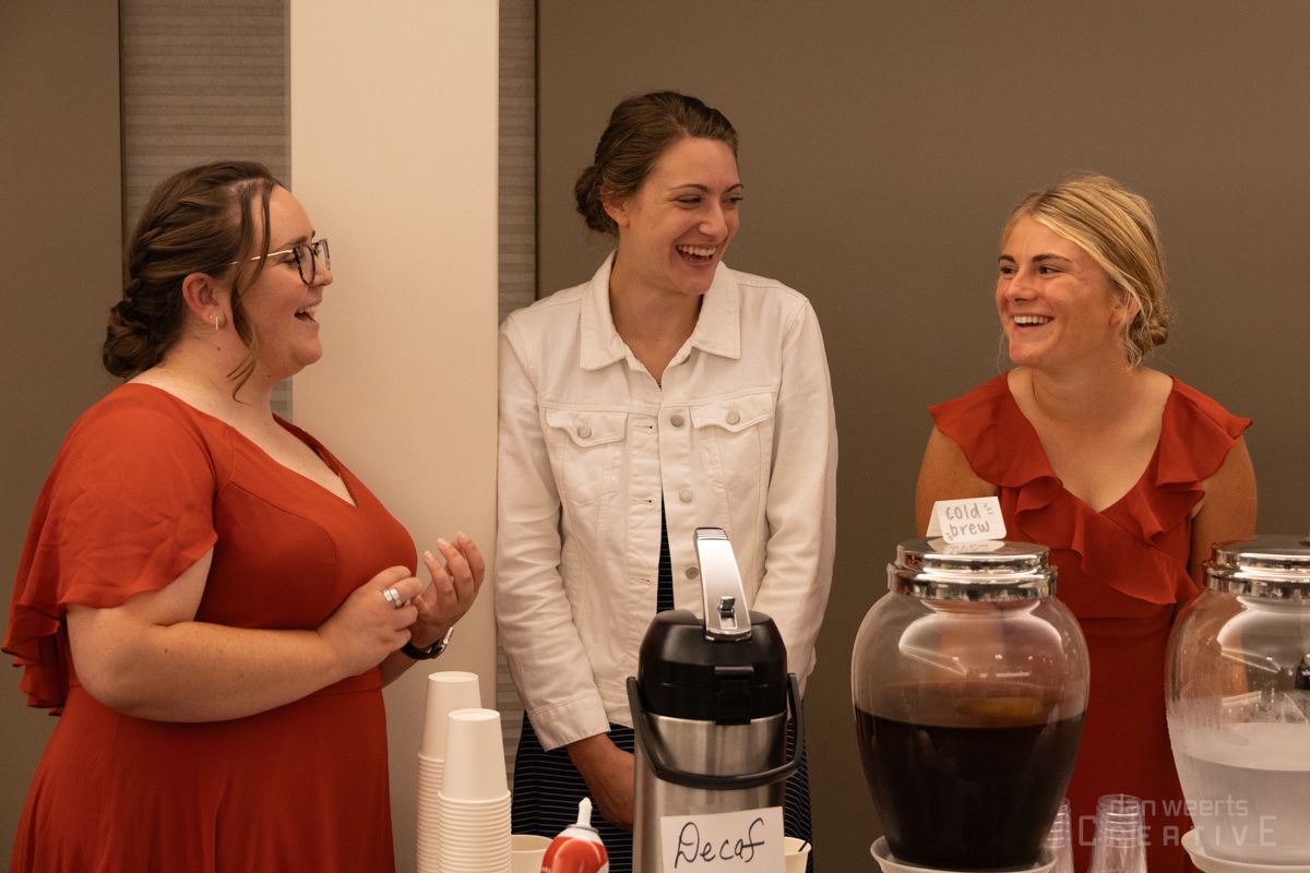 Three women are standing next to each other and laughing in a room.