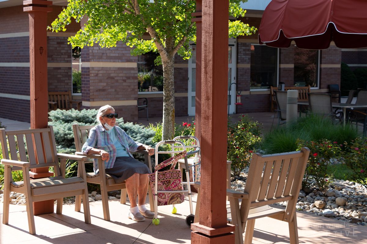 An elderly woman sits on a bench under an awning