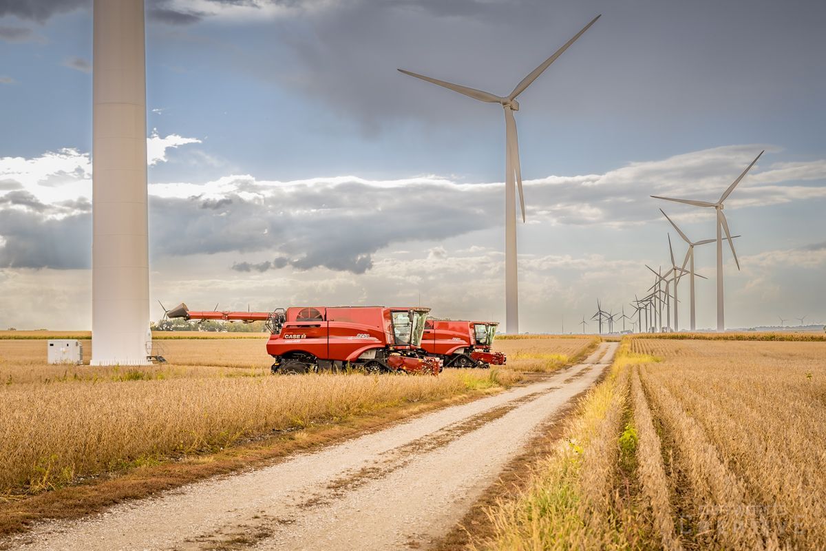 A combine harvester is in a field with wind turbines in the background.