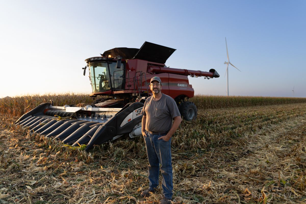 A man is standing in front of a combine harvester in a field.