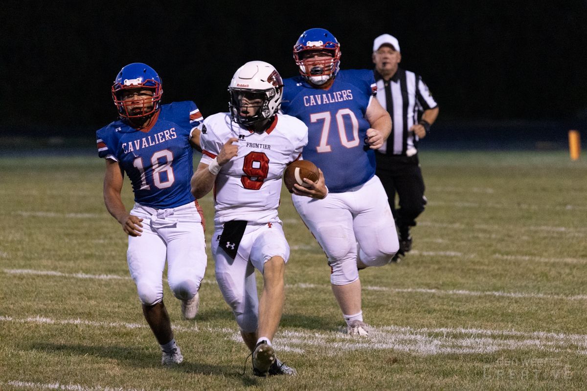 A group of football players are running on a field with a referee in the background.