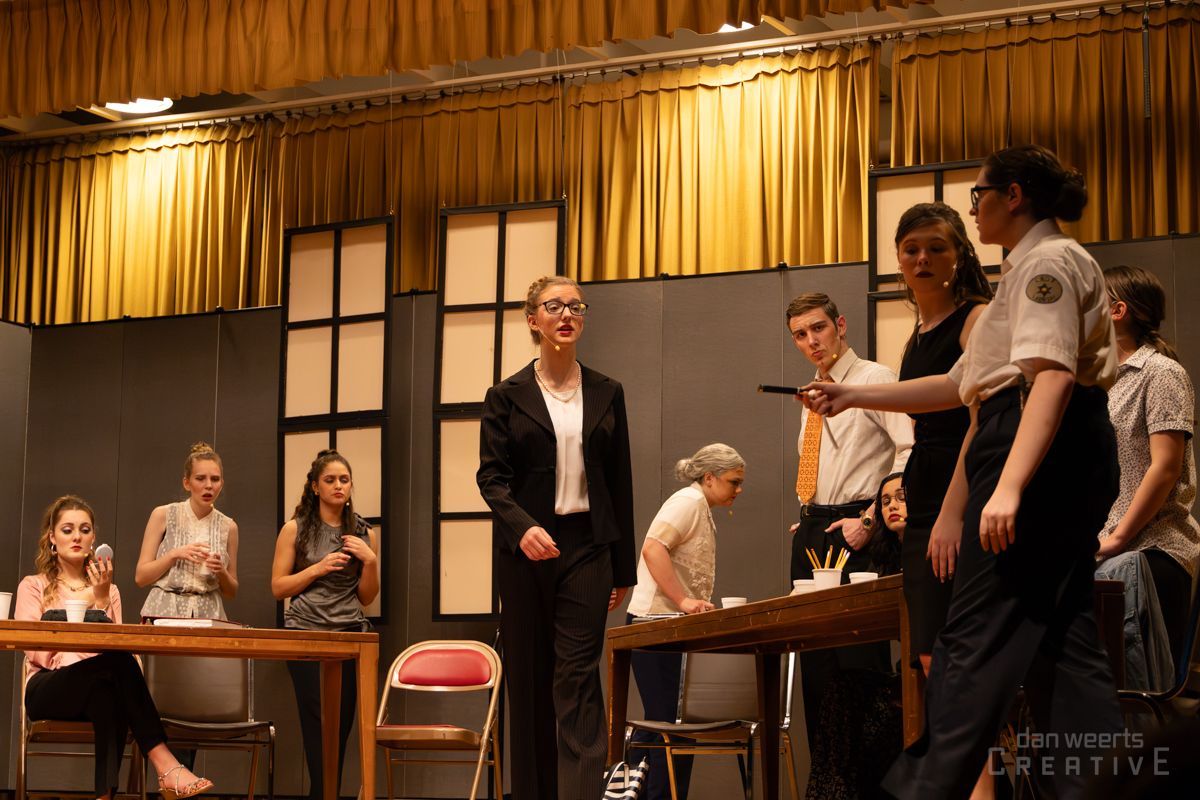 A group of people are standing around a table and a woman is standing in front of them
