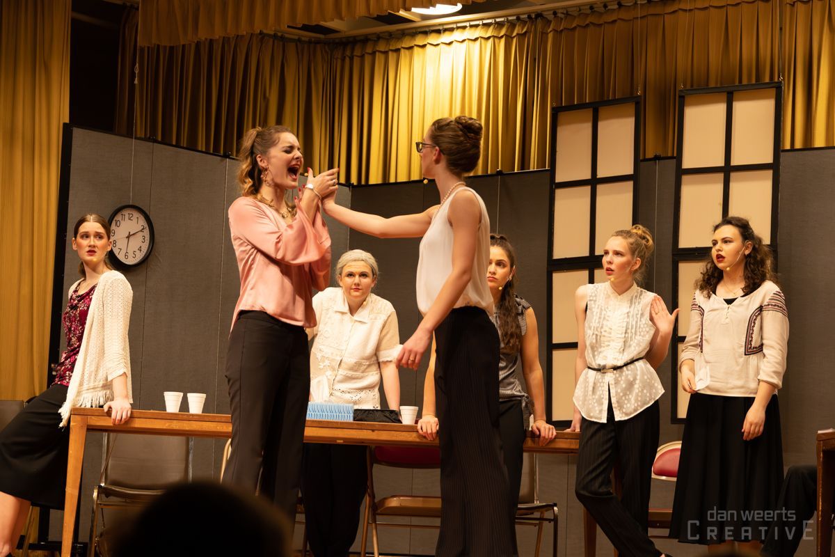 A group of women are standing around a table with a clock on the wall behind them