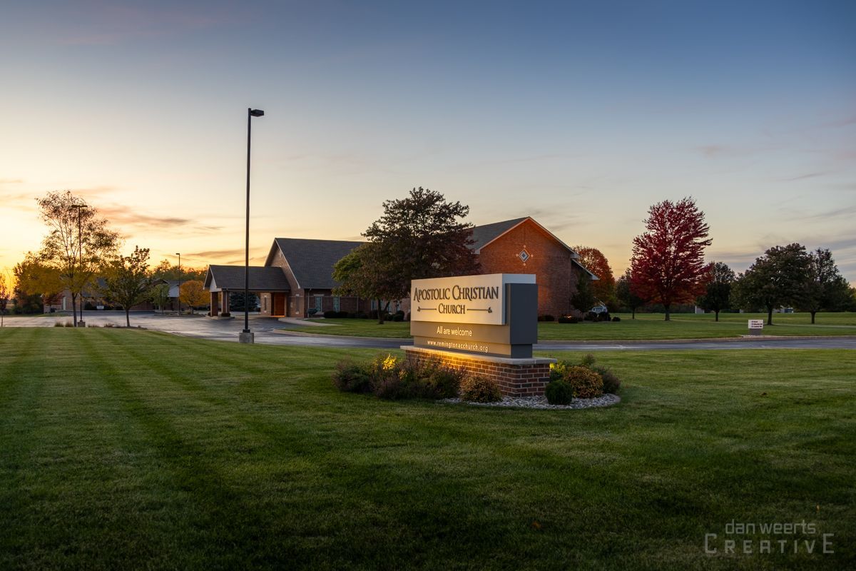 A sign in the middle of a grassy field with a sunset in the background