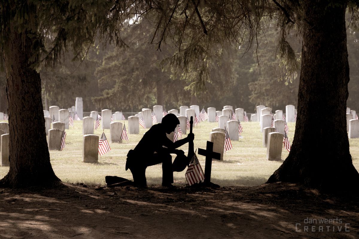 A man is kneeling in front of a grave in a cemetery.