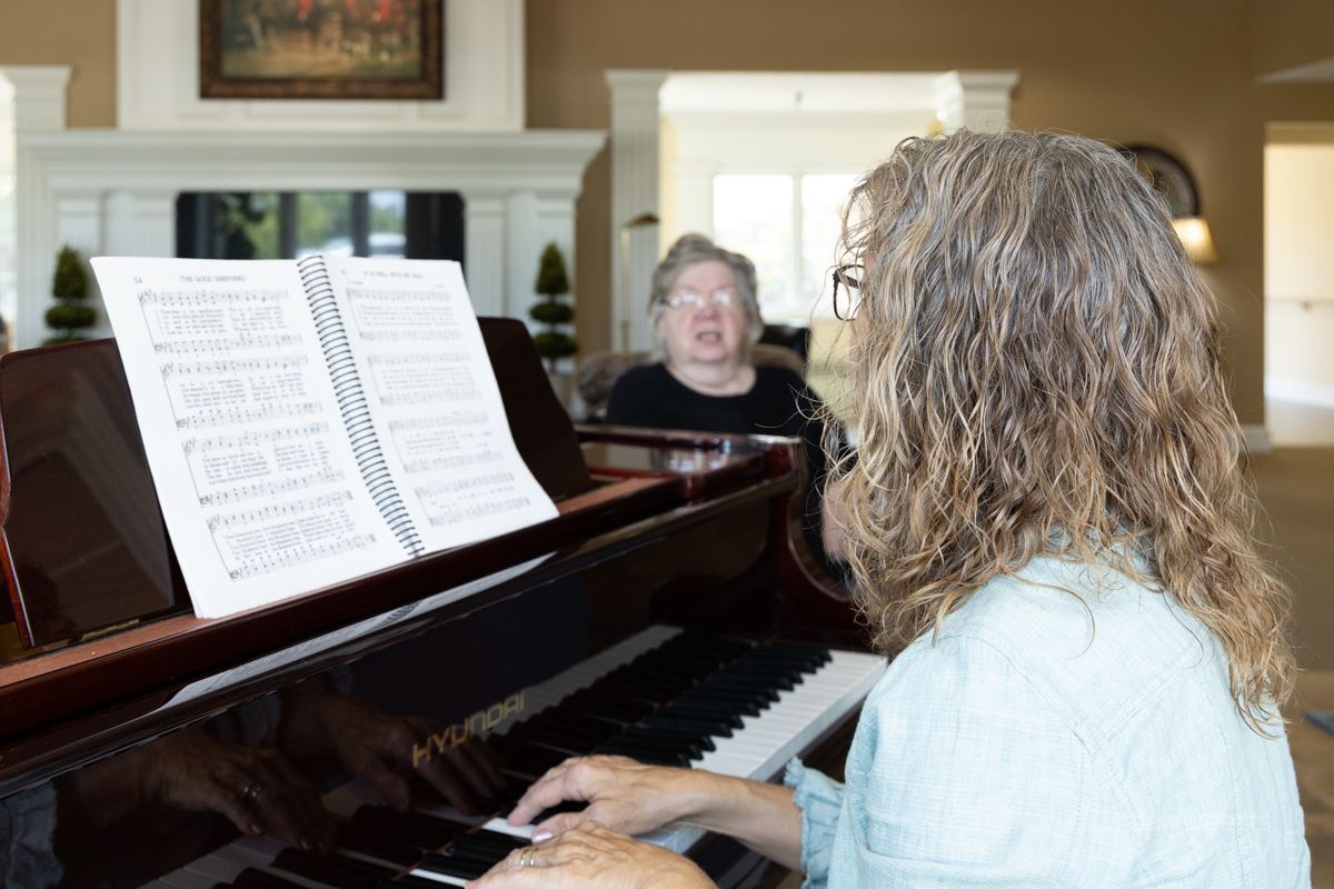 A woman is playing a piano in a living room while another woman watches.