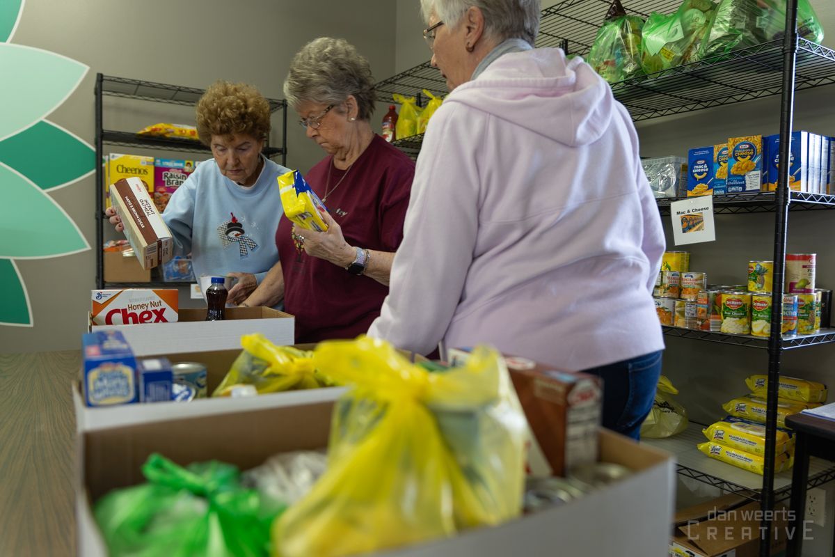 Three women are standing in a store looking at boxes of food.