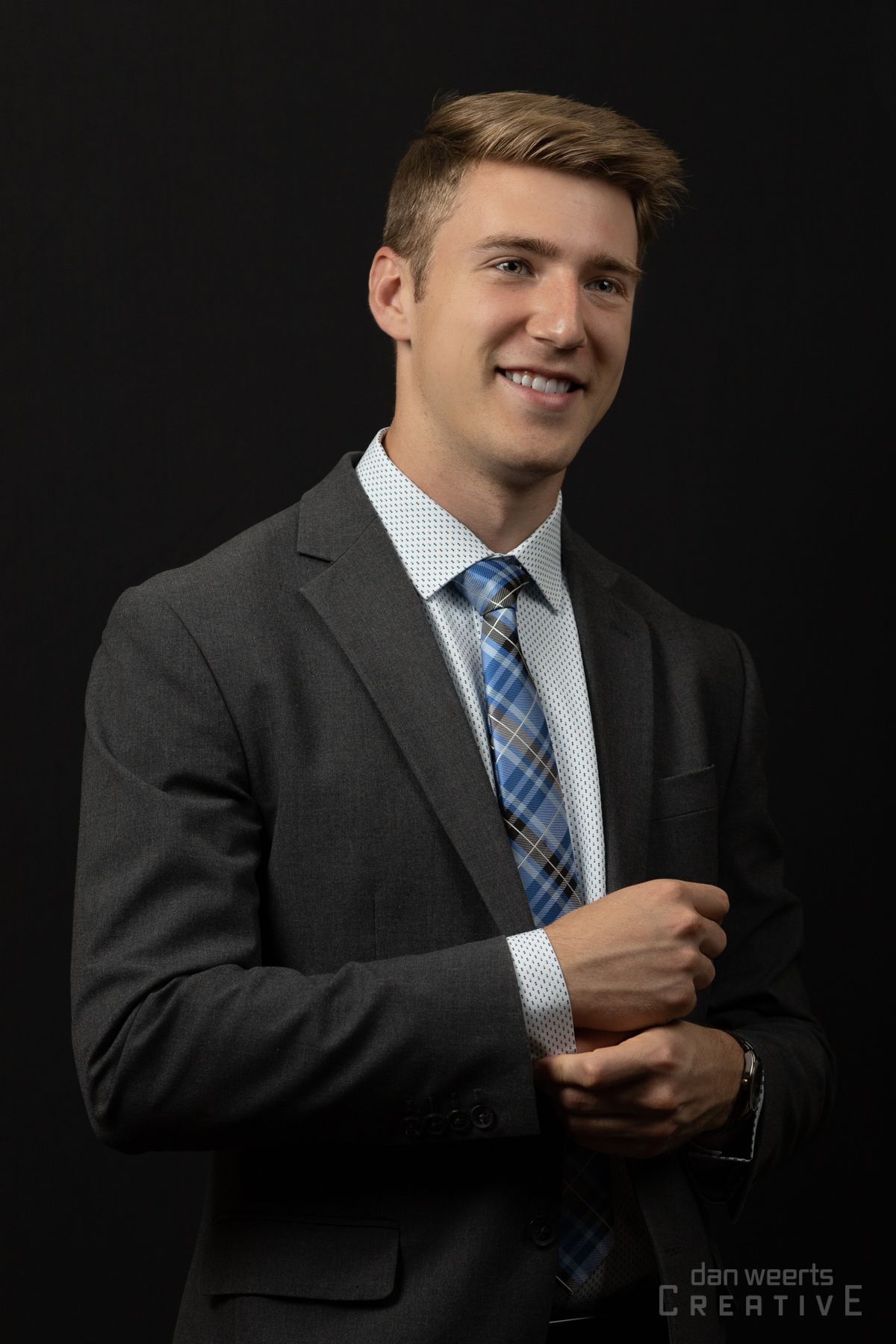 A man in a suit and tie is smiling and adjusting his cufflinks.