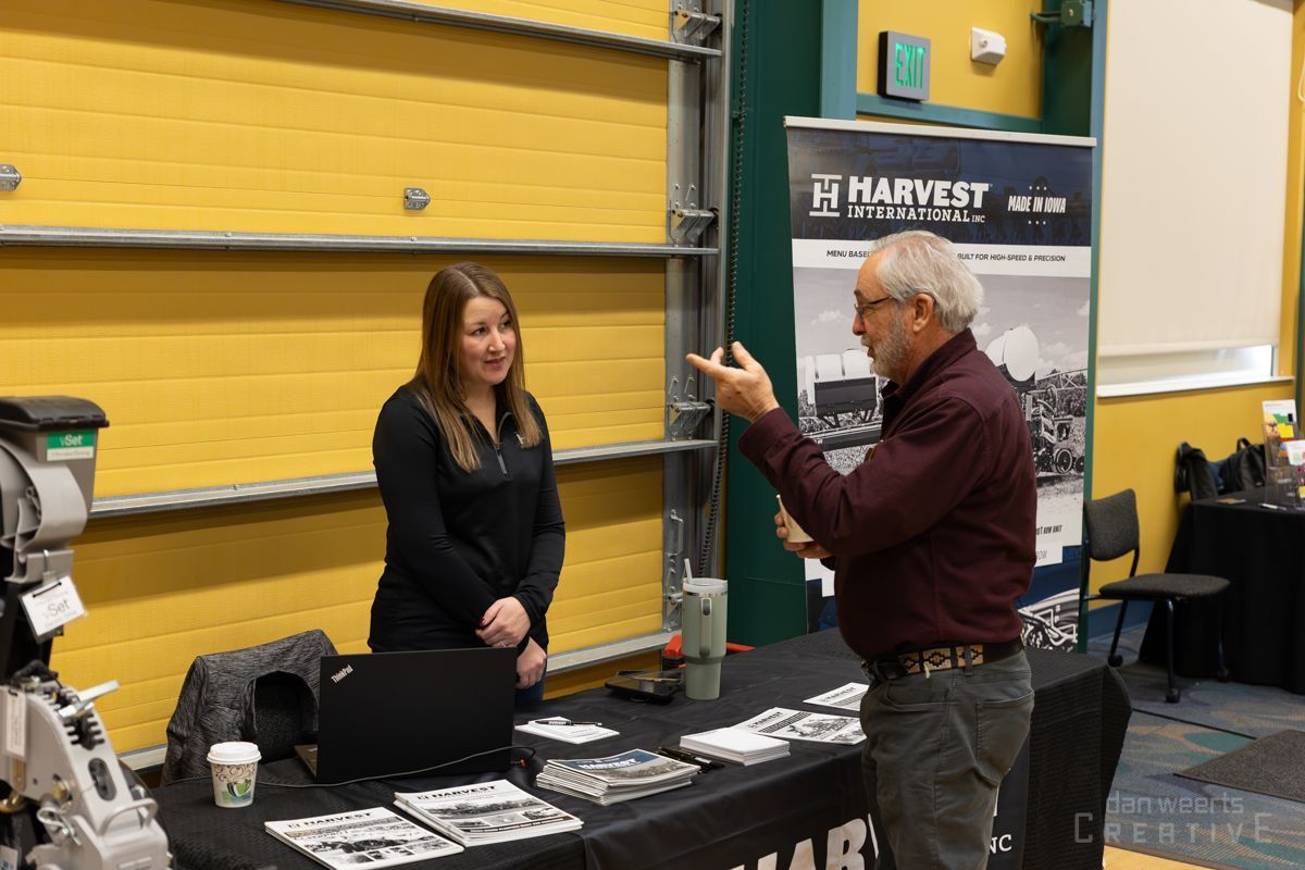 A man and a woman are standing at a table talking to each other.