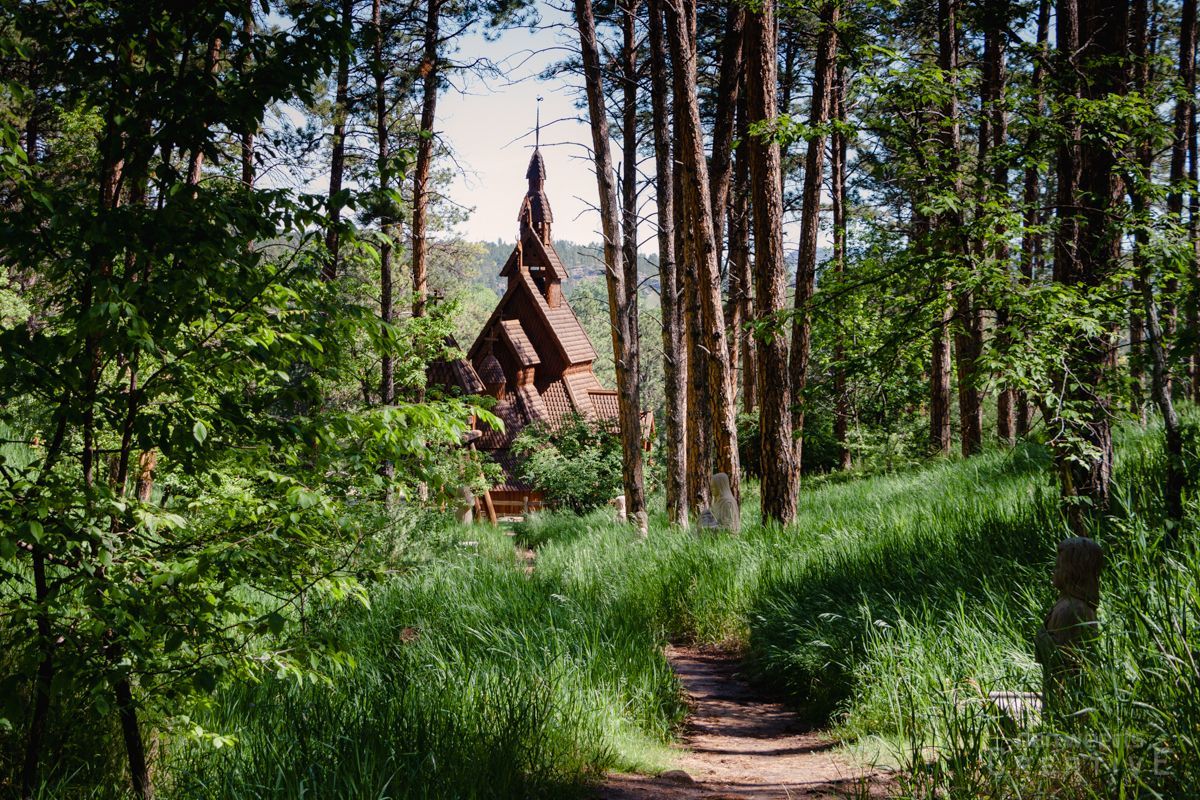 A small wooden church is surrounded by tall trees in the middle of a forest.