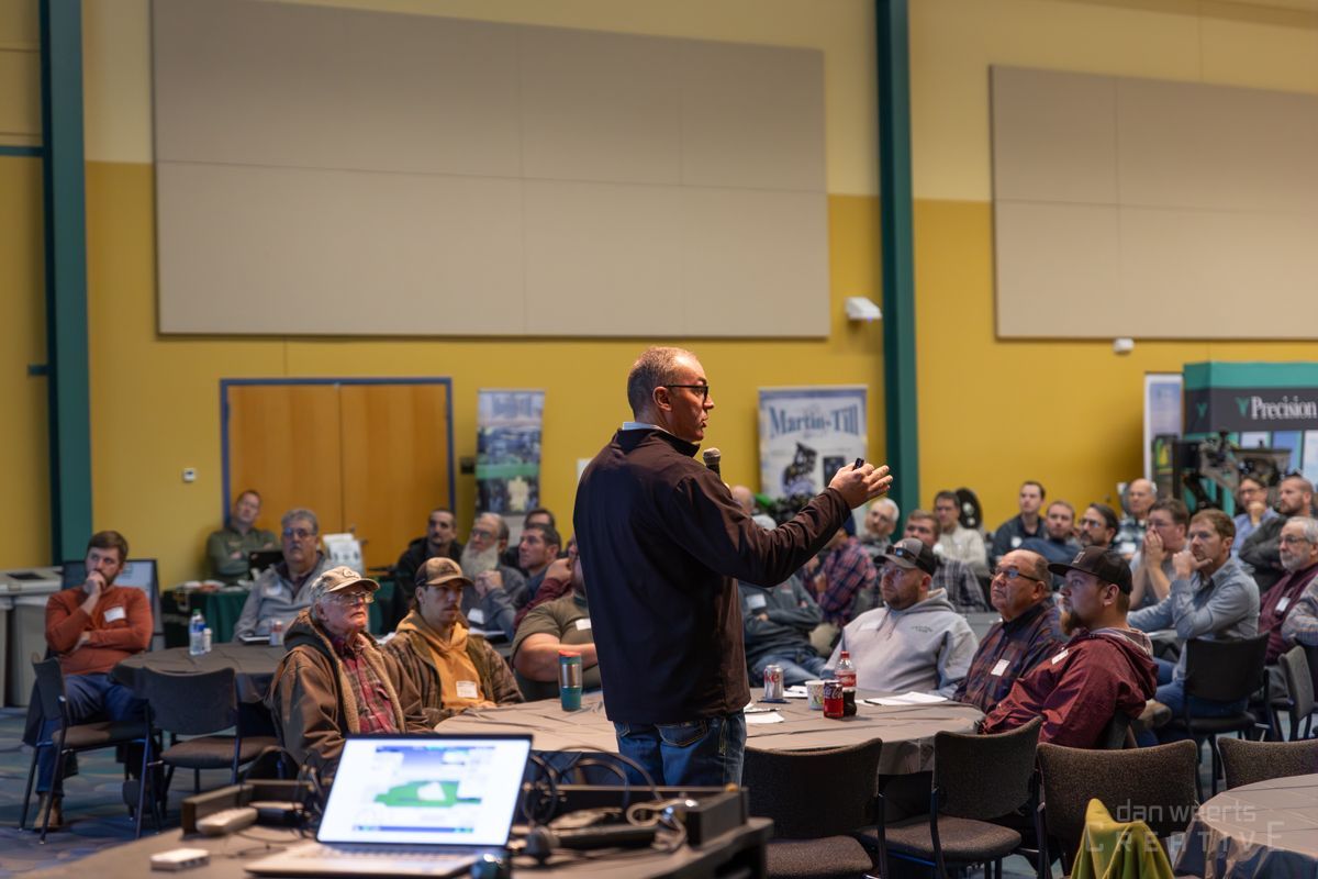 A man is giving a presentation to a group of people sitting at tables.