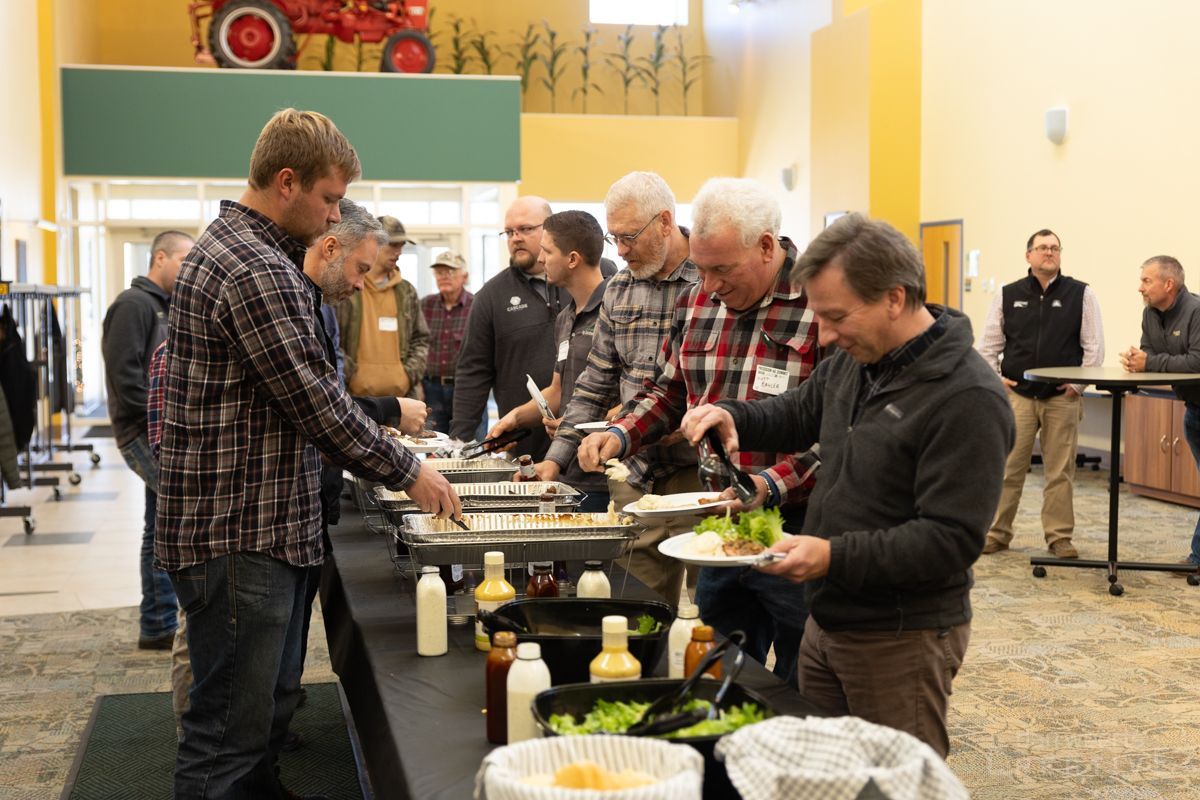 A group of men are standing at a long table getting food.