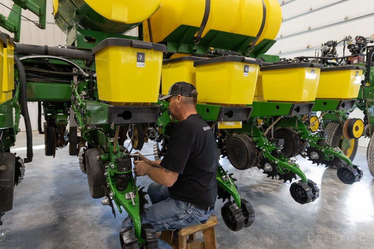 A man is working on a john deere planter in a warehouse.