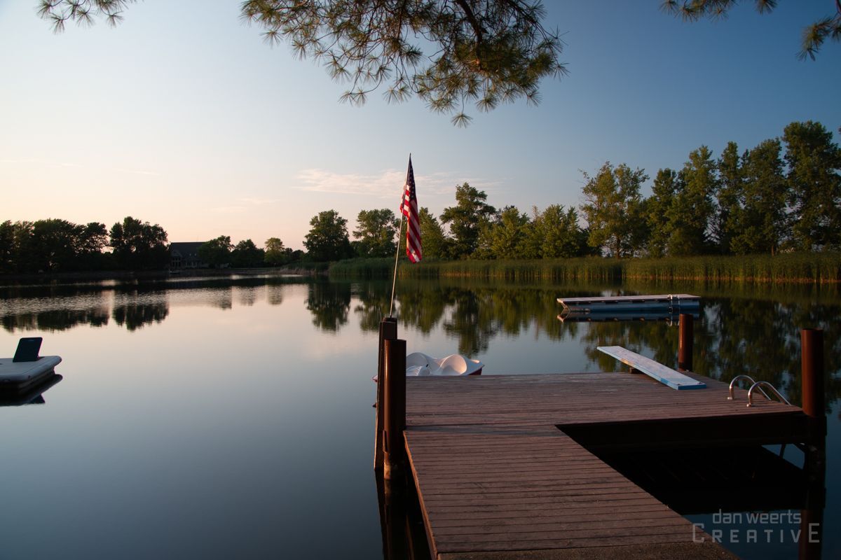 An american flag is flying over a lake with a dock in the foreground