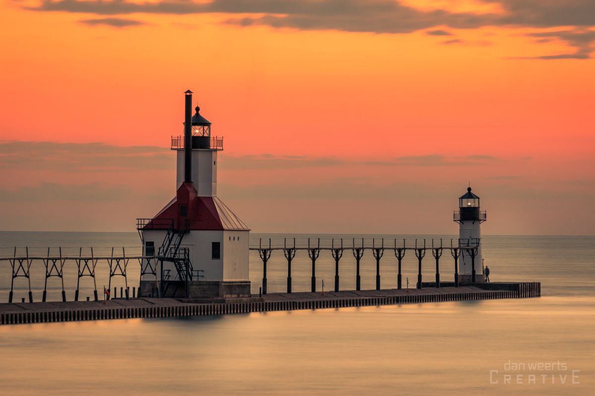 A lighthouse on a pier overlooking the ocean at sunset.