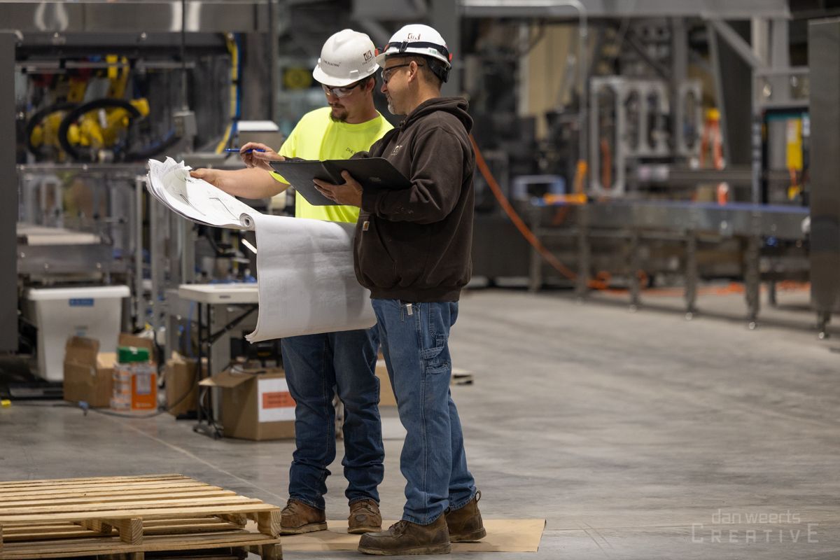 Two men are standing in a factory looking at a blueprint.