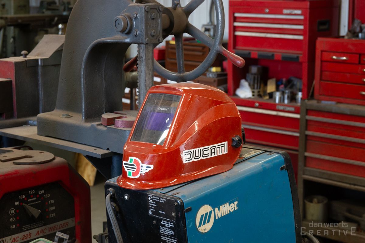 A red miller welding helmet is sitting on top of a blue welding machine.