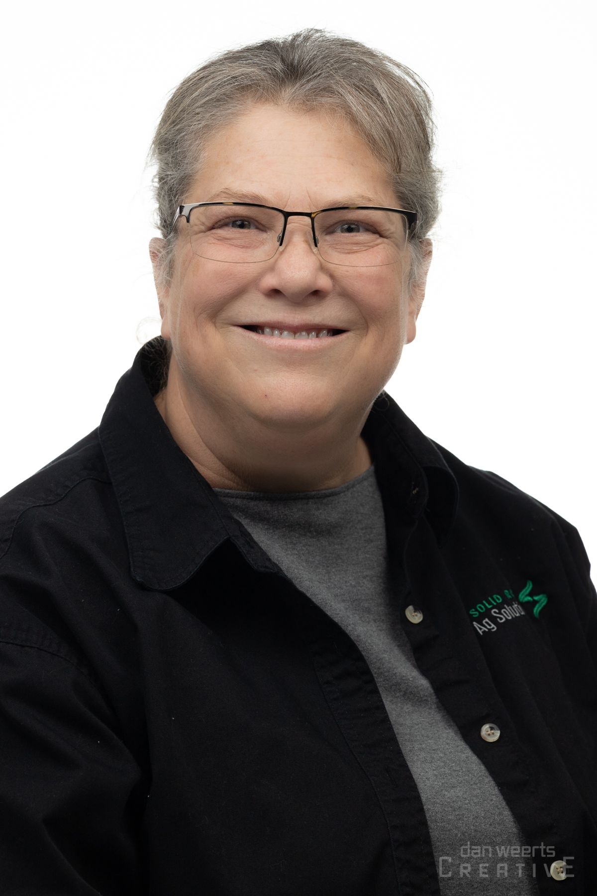 A woman wearing glasses and a black jacket is smiling for the camera.