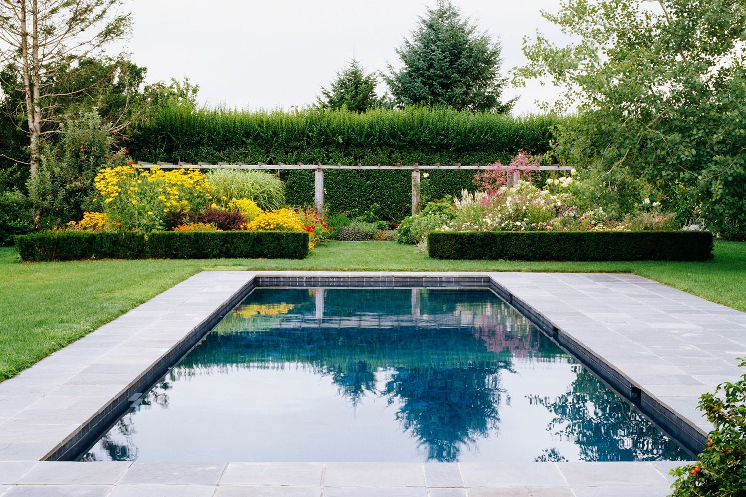 There is a large swimming pool in the middle of a garden.