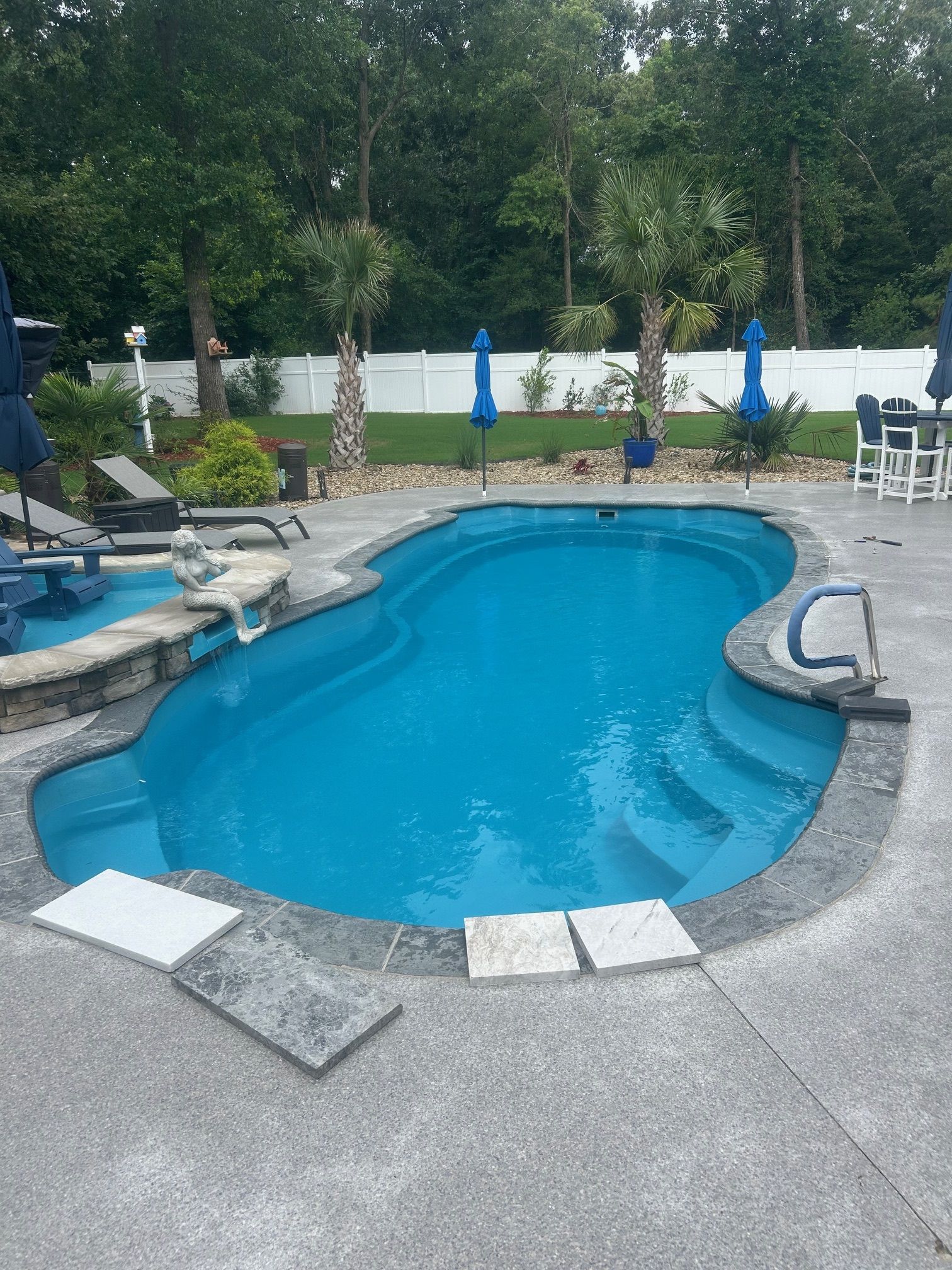 A large blue swimming pool is surrounded by chairs and umbrellas