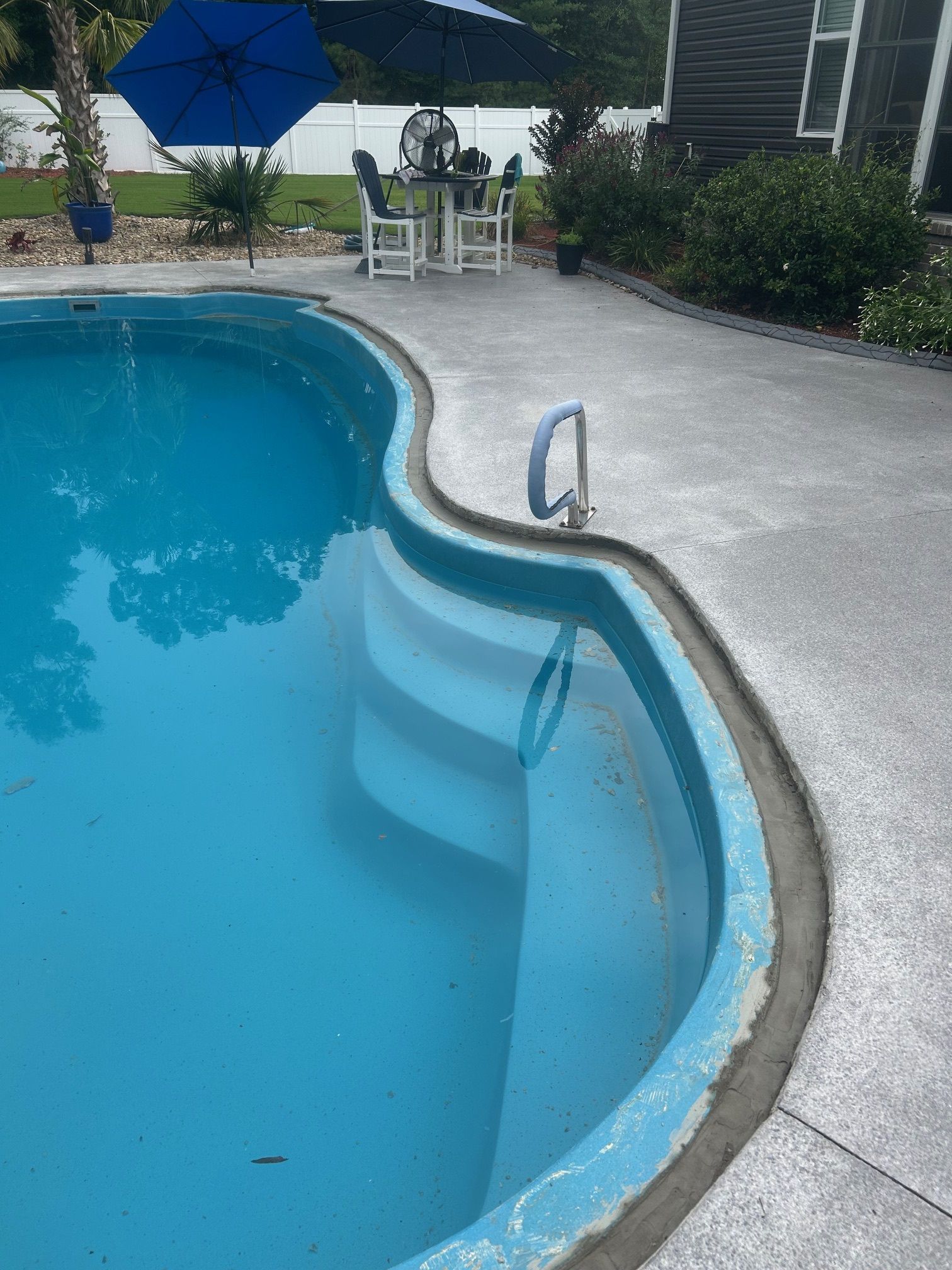 A large swimming pool with a table and chairs in the background.