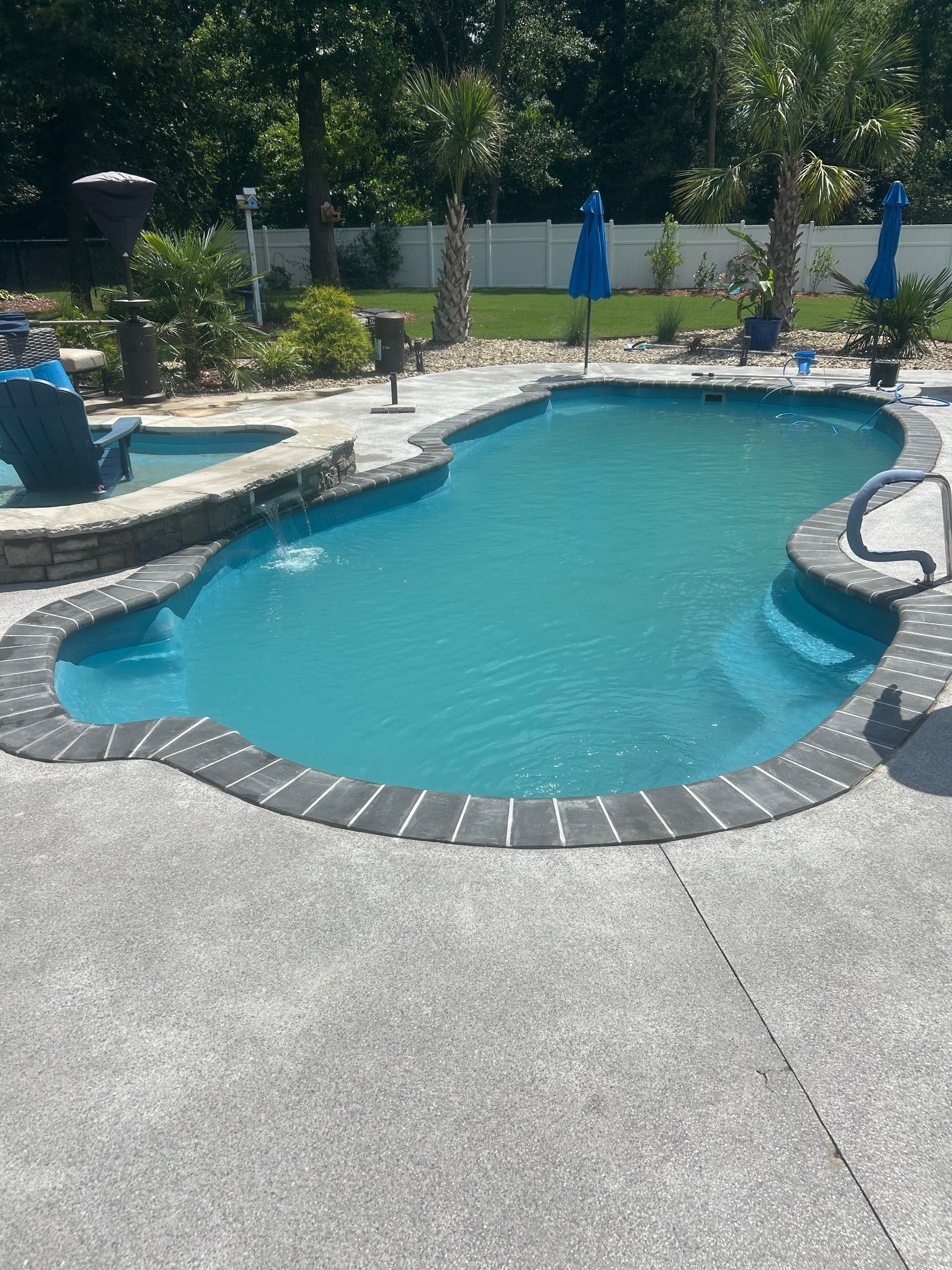 A large swimming pool with blue water and umbrellas in a backyard.