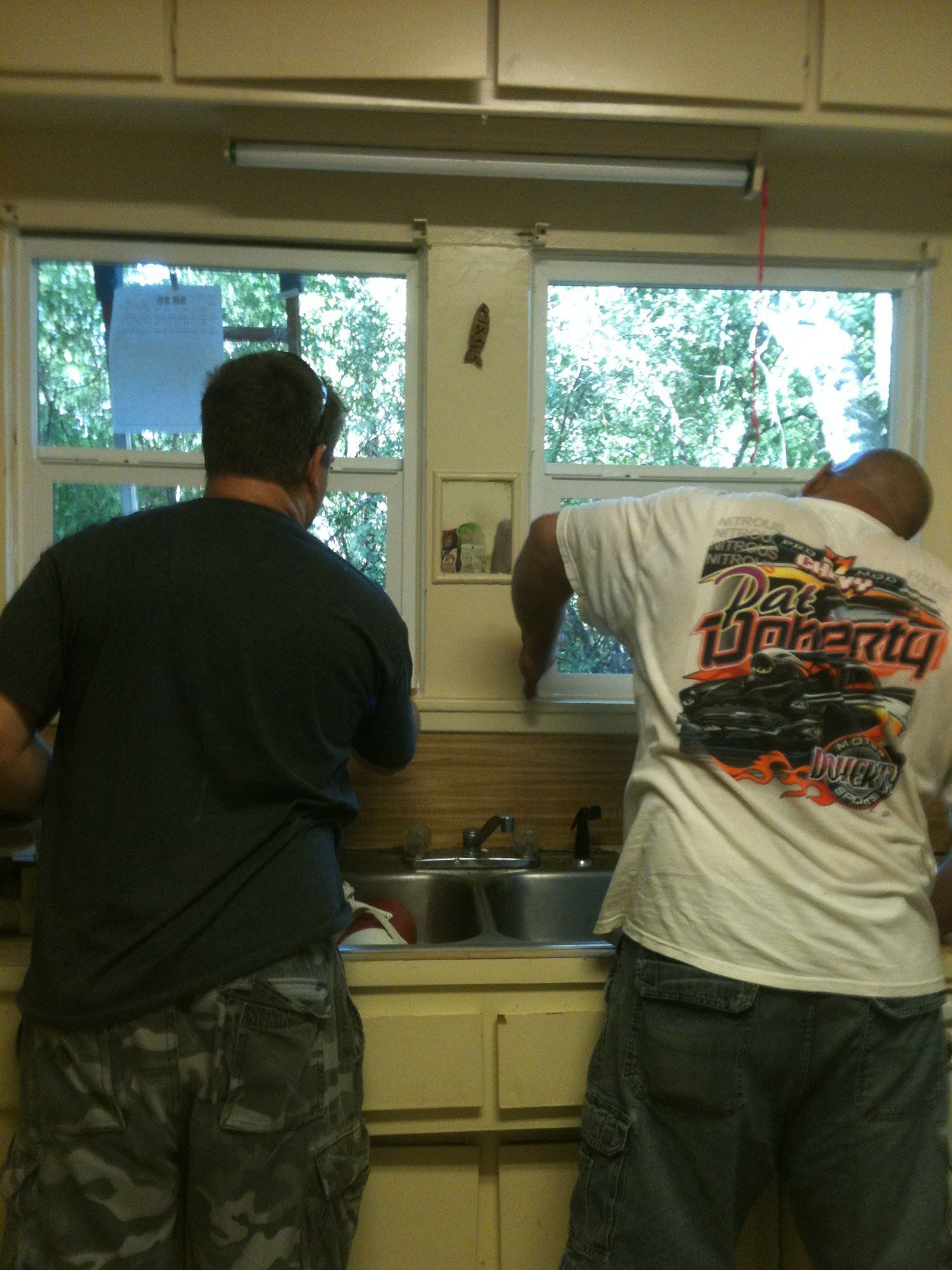 Two men are standing in a kitchen with one wearing a shirt that says liberty