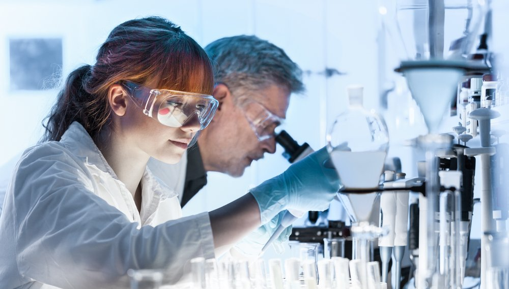 A man and a woman are looking through a microscope in a laboratory.