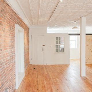 A large empty room with hardwood floors and a brick wall.