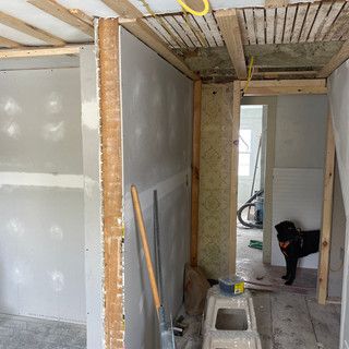 A dog is sitting on a stool in a room under construction.