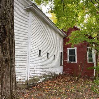 A white house next to a red house with a tree in front of it.