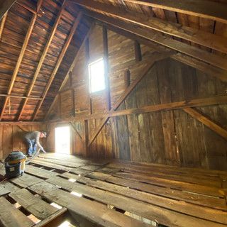 A man is cleaning the floor of an attic with a vacuum cleaner.